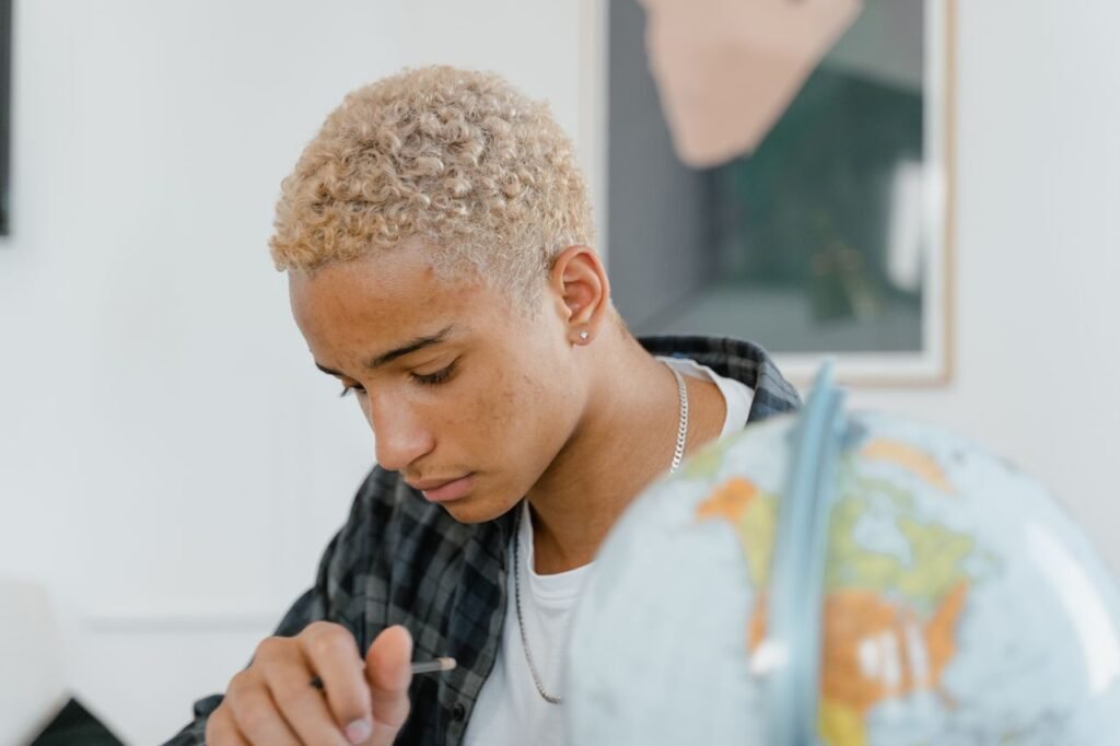 Curly-haired young man focuses on geography study indoors with a globe.