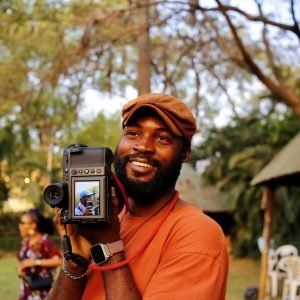 pexels-photo-30517382-30517382 Smiling African photographer with camera outdoors in Abuja park. Captured amidst nature.